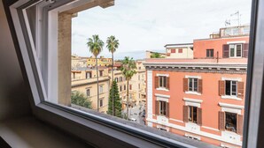 Une vue depuis une fenêtre à cadre blanc, donnant sur une rue bordée d’immeubles et de palmiers.