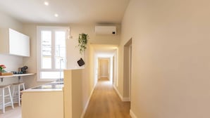 Un couloir étroit avec un coin cuisine d’un côté, comprenant un plan de travail, des tabourets et une plante suspendue.
