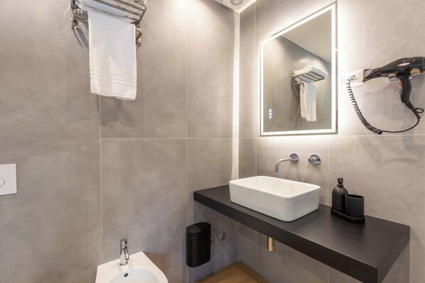A modern bathroom with a white sink, a mirror, and a hairdryer on the wall.