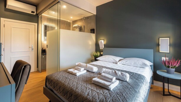 Une chambre d’hôtel moderne dotée d’un grand lit, d’un bureau et d’une salle de bain visible à travers une paroi en verre.