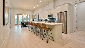 A modern kitchen with a central island, stainless steel appliances, and a dining area with bar stools. - Angels Retreat @ Beach Club! (Gulf Shores)