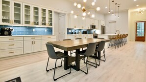 A modern kitchen with white cabinets, a wooden dining table, and a chandelier. - Angels Retreat @ Beach Club! (Gulf Shores)