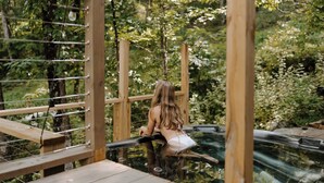 Una terrazza in legno con una persona seduta su una panchina, immersa nel verde.