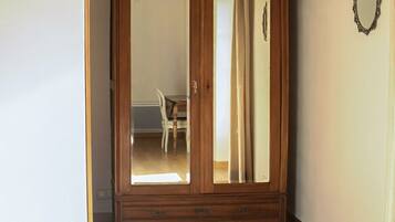 A room with a wooden wardrobe, a bed, and a mirror on the wall.