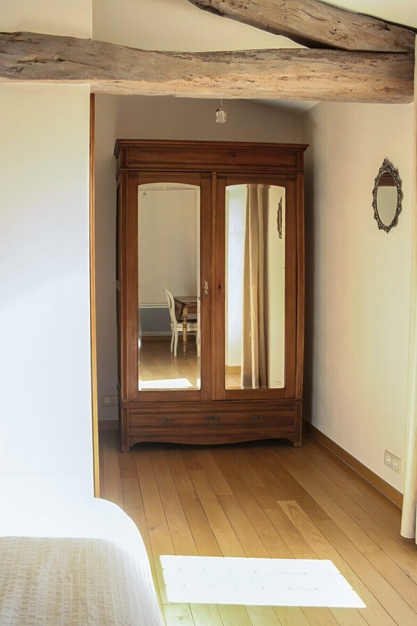 A room with a wooden wardrobe, a bed, and a mirror on the wall.