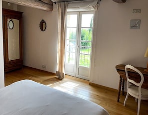 A bedroom with a bed, a wooden desk, a chair, a window with curtains, and a door with a mirror.