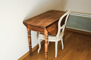 Una mesa de madera para comer con una silla blanca, ubicada frente a una pared blanca y piso de madera.