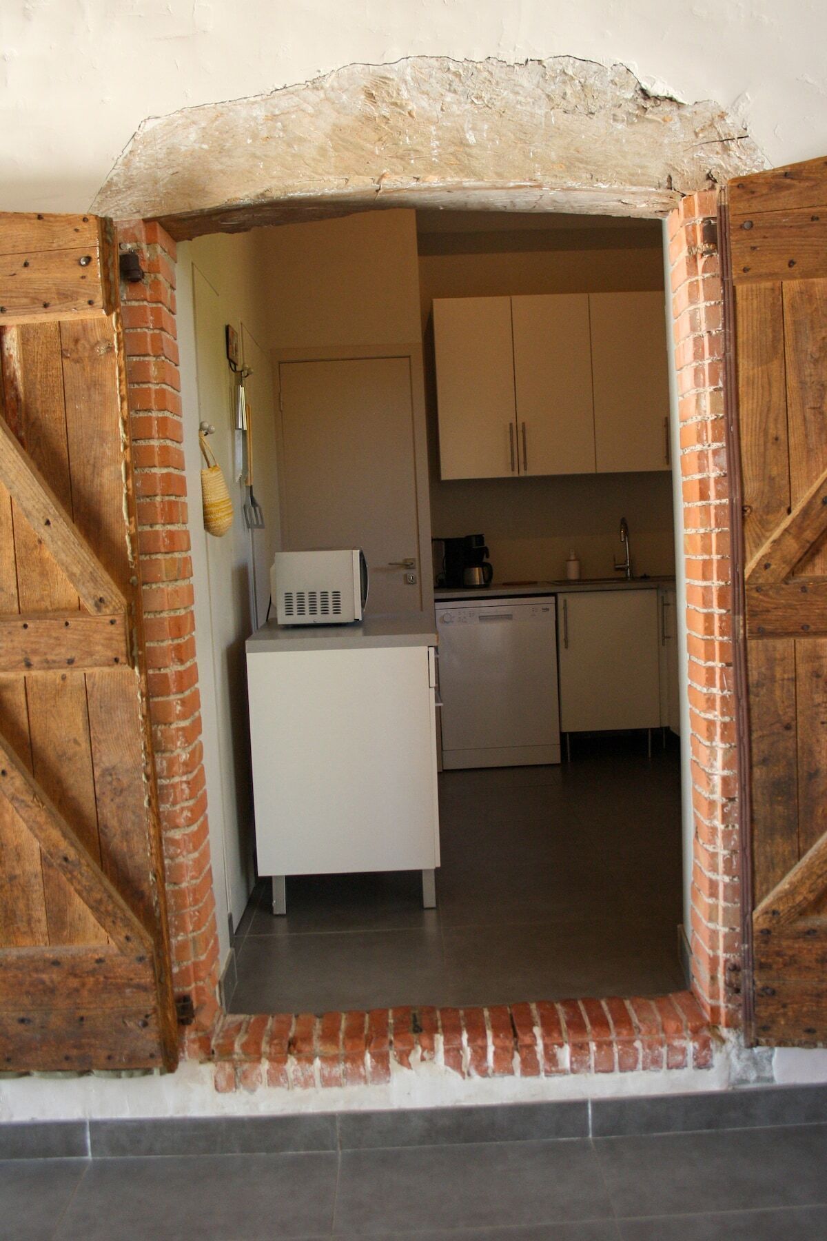 Een kleine keuken met witte kastjes, een magnetron en een koffiezetapparaat.