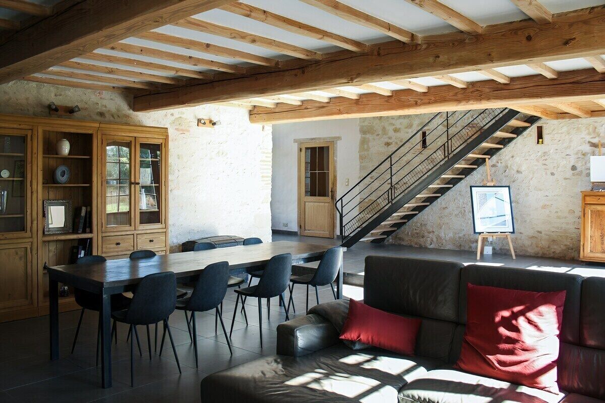 Un intérieur rustique comprenant un coin repas, un escalier et un canapé agrémenté d’un coussin rouge.