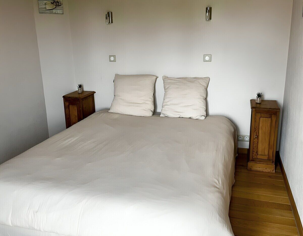 A bed with a white bedspread and two pillows, flanked by two wooden nightstands with small decorative items.
