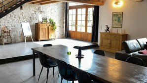 Ein geräumiges Zimmer mit einem großen Holztisch, schwarzen Stühlen, einer Treppe und einer rustikalen Steinwand.
