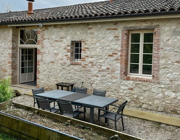 A rustic stone building with a tiled roof, a large table with chairs, and a small window. - 3-star holiday cottage in a barn with swimming poo (Fiac)