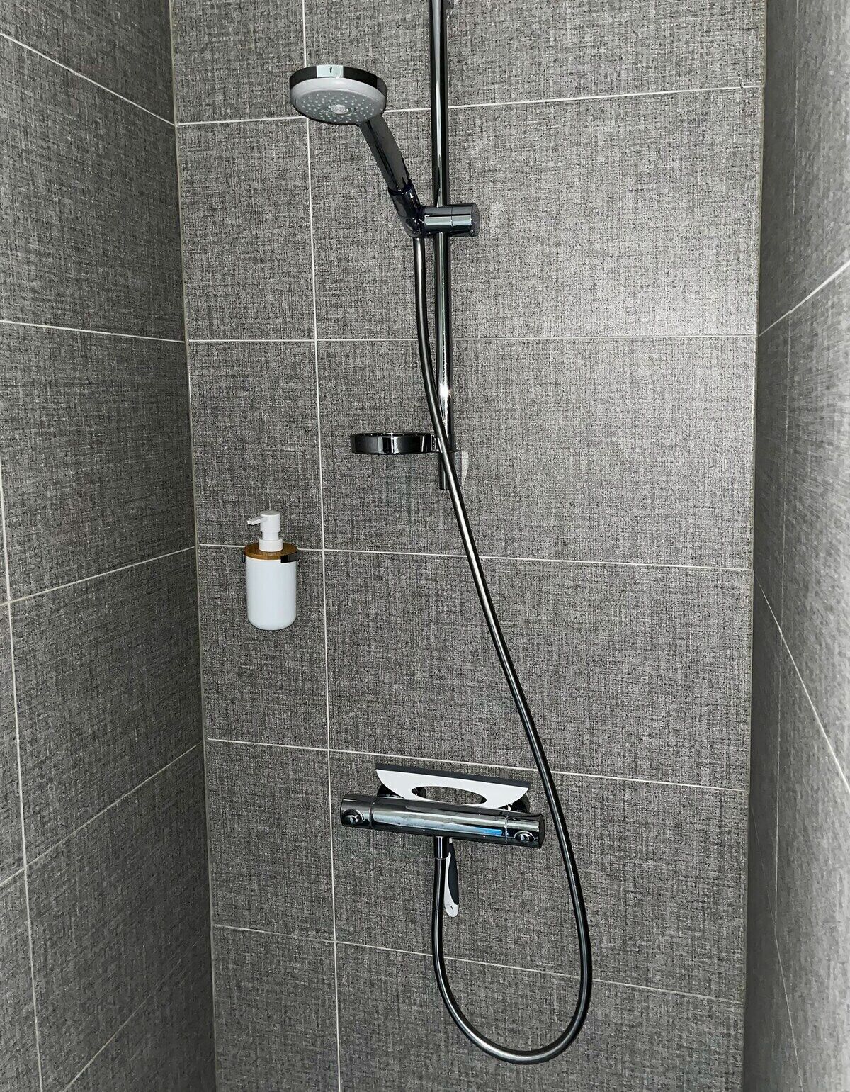 A modern shower with a handheld showerhead, a handheld shower attachment, and a wall-mounted faucet.