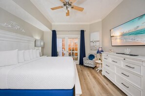 Une chambre d’hôtel avec un grand lit, un ventilateur de plafond, une télévision, une commode et une vue sur la plage.