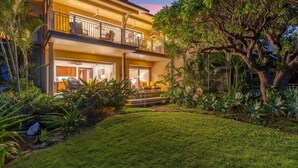 A two-story building with a well-maintained lawn, outdoor seating area, and a large tree in the foreground. - Luxury 3BR Ka 'Ulu Villa 129B at Hualalai – Island Elegance & Golf Views (Kailua Kona)
