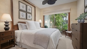 A bedroom with a large bed, a nightstand, a dresser, and a window with a view of greenery. - Luxury 3BR Ka 'Ulu Villa 129B at Hualalai – Island Elegance & Golf Views (Kailua Kona)