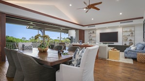 A spacious living area with a dining table, comfortable seating, a television, and a view of the outdoors. - Luxury 3BR Ka 'Ulu Villa 129B at Hualalai – Island Elegance & Golf Views (Kailua Kona)
