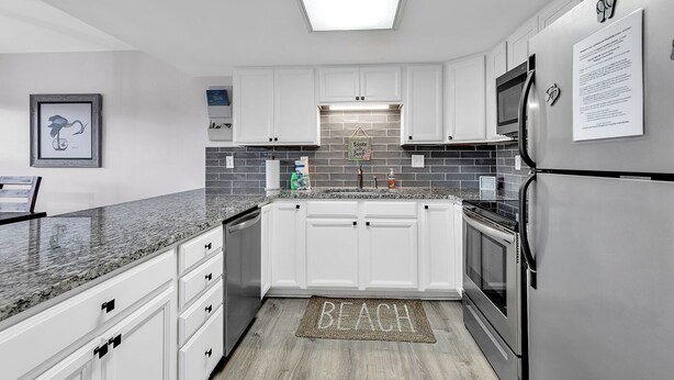 A modern kitchen with white cabinets, a granite countertop, a stainless steel refrigerator, and a backsplash. - Gorgeous modern condo with unmatched view looking out over the pool! (Surfside Beach)
