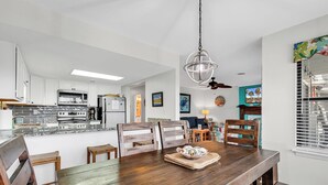 A modern kitchen with white cabinets, stainless steel appliances, and a wooden dining table with chairs. - Gorgeous modern condo with unmatched view looking out over the pool! (Surfside Beach)