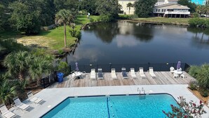 A pool area with a wooden deck, lounge chairs, and a view of a lake and surrounding greenery. - Gorgeous modern condo with unmatched view looking out over the pool! (Surfside Beach)