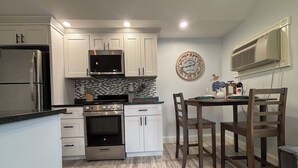 A modern kitchen with white cabinets, stainless steel appliances, and a wooden dining table with chairs. - The Nautical Nest-Belle of Maine (Wells)