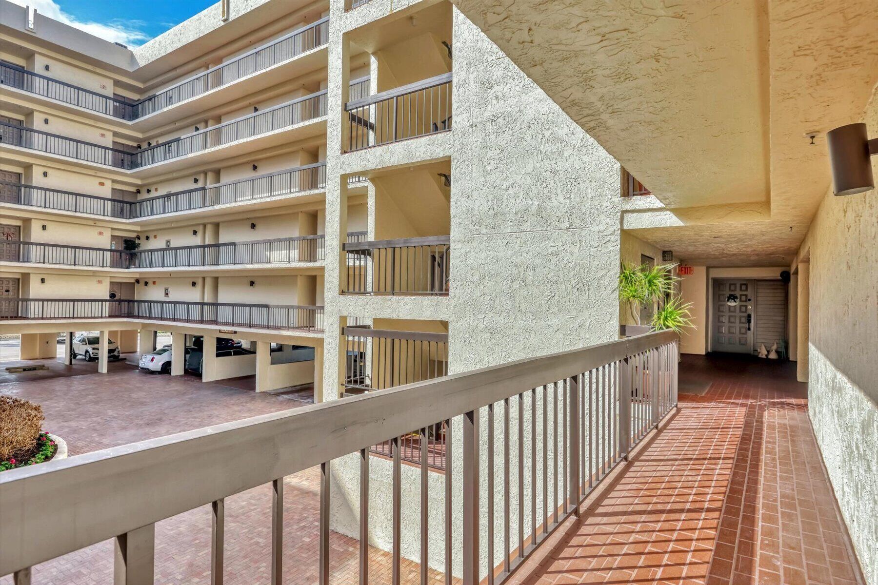 A multi-story building with balconies, a covered walkway, and a parking area.