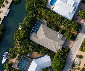 Vista aérea de um resort com um edifício central cercado por palmeiras, um píer com um barco e uma piscina.