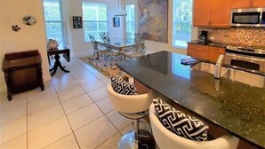 A modern kitchen with a central island, stainless steel appliances, and a dining area with chairs and a table. - 4/3 Canal Front Condo, Private Pool, Dock (Longboat Key)