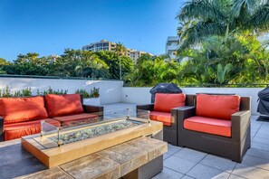 An outdoor seating area with wicker furniture and red cushions, a glass-top table, and a built-in fire feature. - Beachfront 2 BR / 2 BA  At Players Club By FVC (Longboat Key)