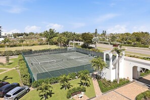 A tennis court surrounded by greenery and a white building with arches. - Beachfront 2 BR / 2 BA  At Players Club By FVC (Longboat Key)