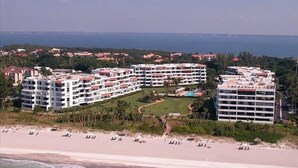 Et hotel ved stranden med flere bygninger, en swimmingpool og en strand i forgrunden.