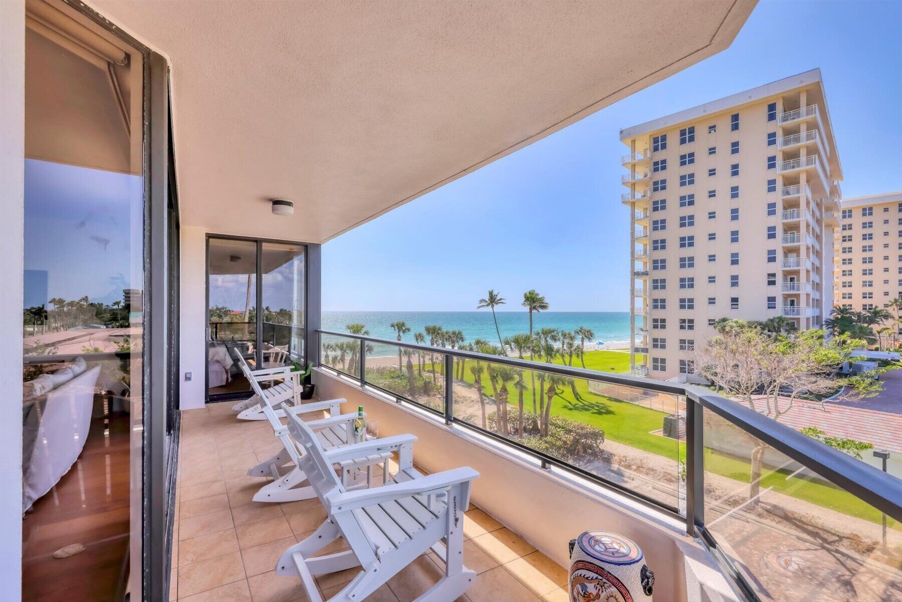 A balcony with white chairs, a view of the ocean, and a tall building in the background.