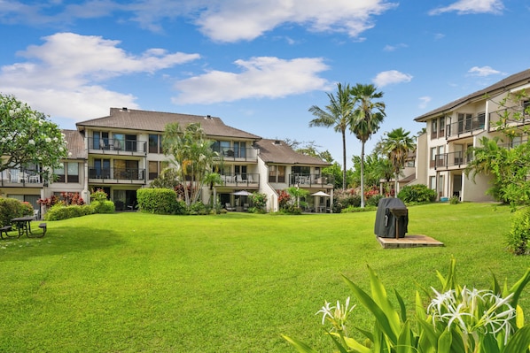 A residential building with multiple balconies, a well-maintained lawn, and a barbecue grill.