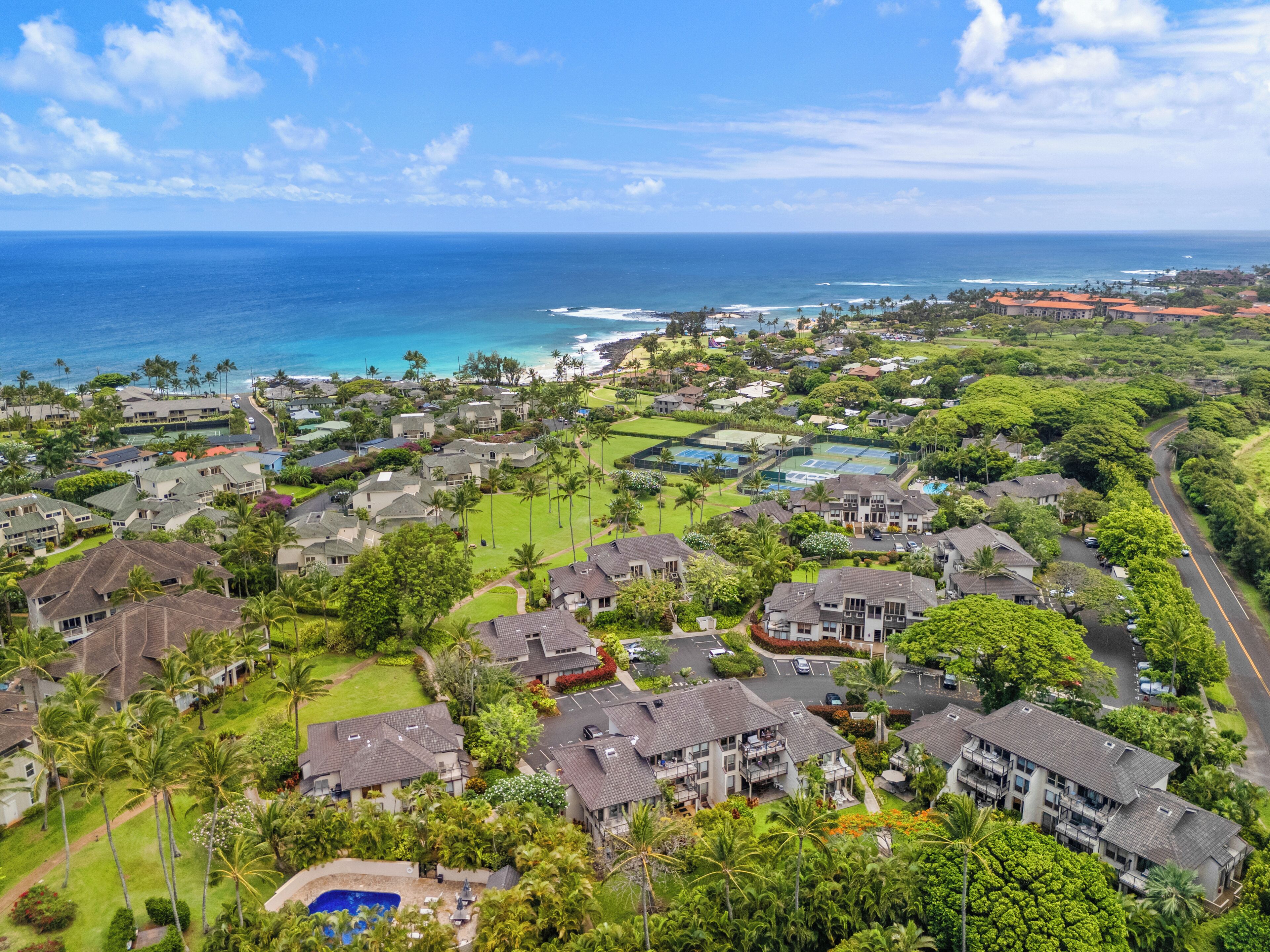 Aerial view of a coastal resort community nestled between lush tropical landscapes and pristine oceanfront, showcasing residential neighborhoods with nearby beach access and scenic natural surroundings.