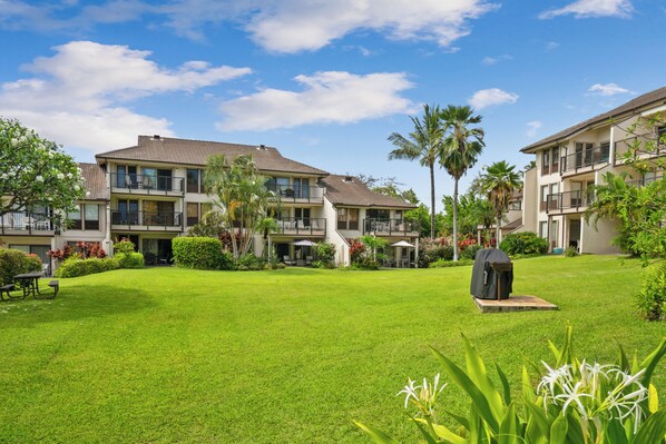 A residential building with multiple balconies, a well-maintained lawn, and a barbecue grill.