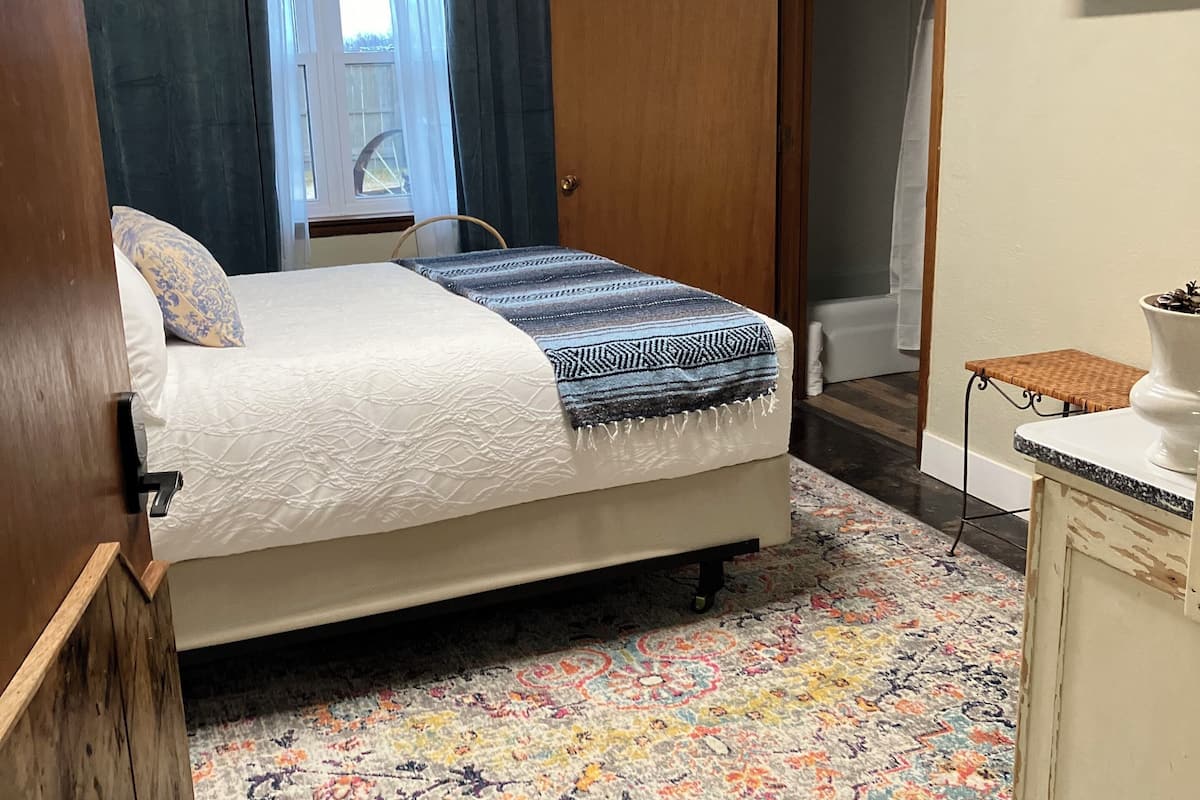 Quarto com cama, tapete colorido, guarda-roupa de madeira e televisão na parede.