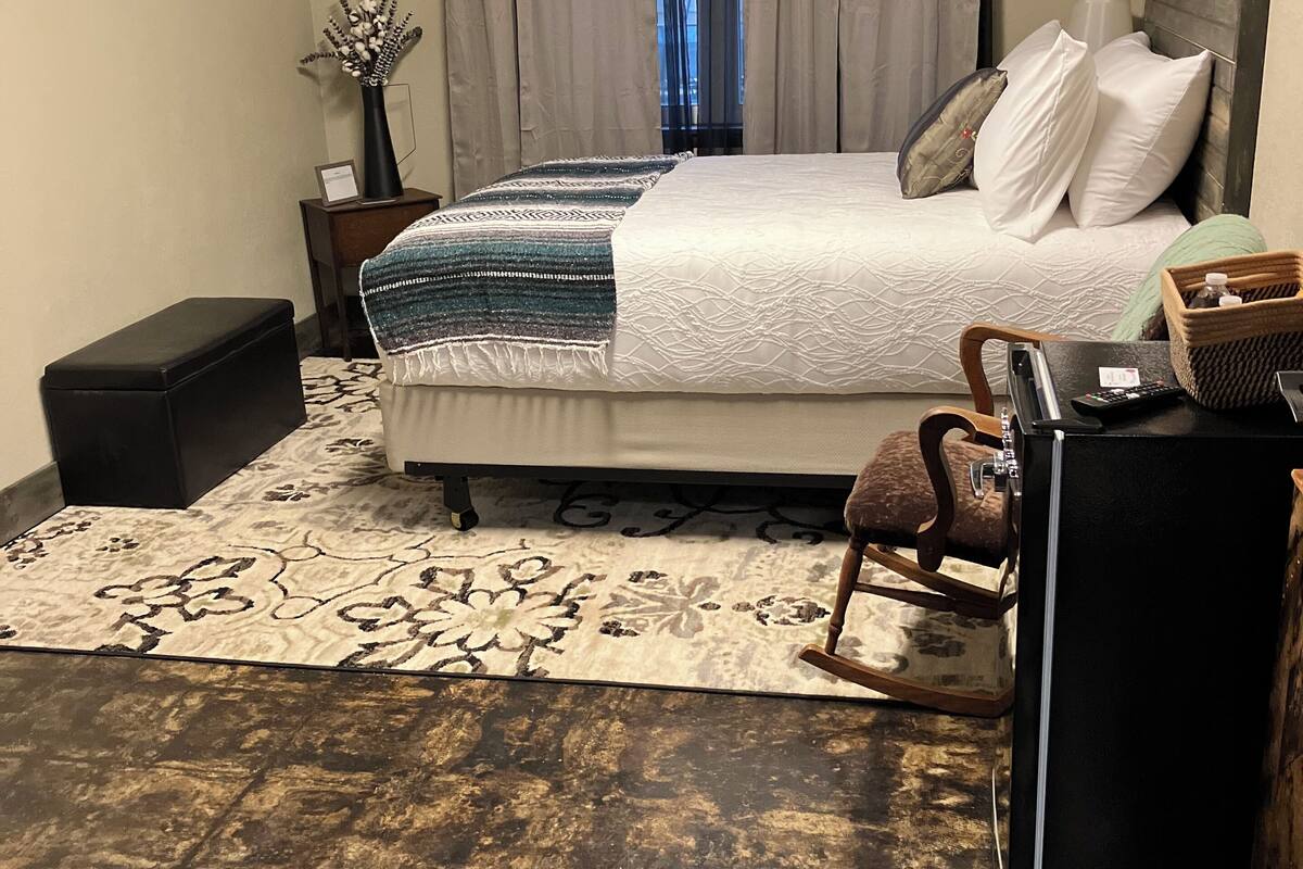 Quarto com cama, mesa de cabeceira, abajur e tapete pequeno.