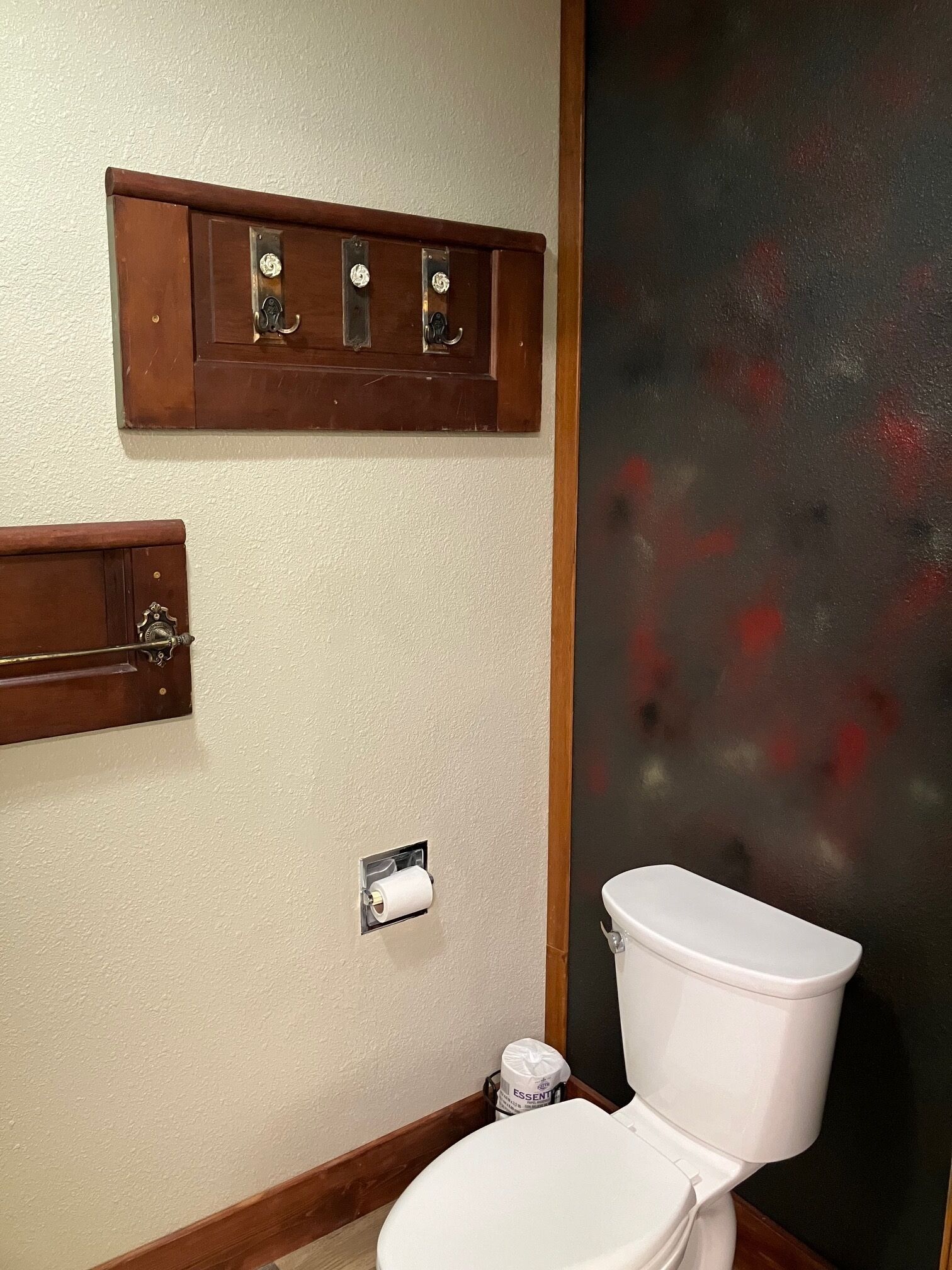Une salle de bain comprenant des toilettes, une étagère en bois avec un distributeur de serviettes et un porte-rouleau de papier toilette.