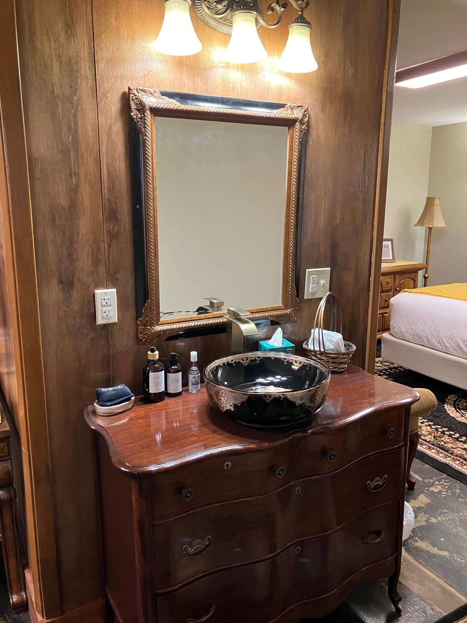 A wooden vanity with a large mirror, a bowl sink, and toiletries.
