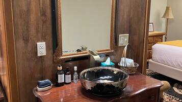 A wooden vanity with a large mirror, a bowl sink, and toiletries.