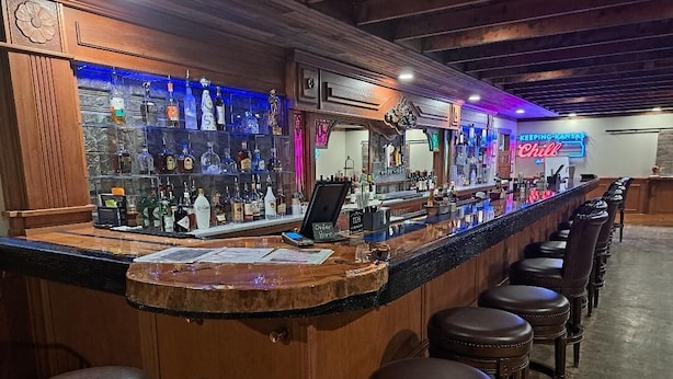 Un espace bar doté d'un long comptoir, de nombreux tabourets et d'une enseigne au néon.