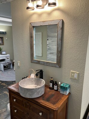 A bathroom with a round marble sink, wooden vanity, and a mirror with a distressed frame.