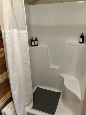 A shower area with a white shower curtain, two bottles of body wash, and a dark bath mat.