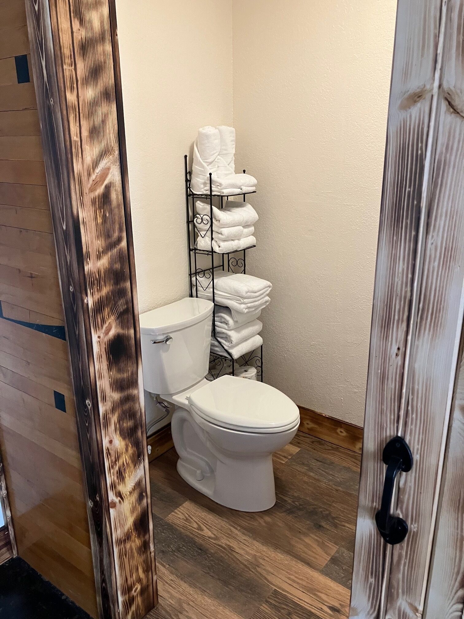 Une salle de bain avec des toilettes blanches, un porte-serviettes où sont soigneusement pliées les serviettes, et un plancher en bois.