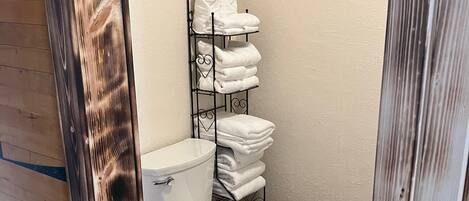 Une salle de bain avec des toilettes blanches, un porte-serviettes où sont soigneusement pliées les serviettes, et un plancher en bois.