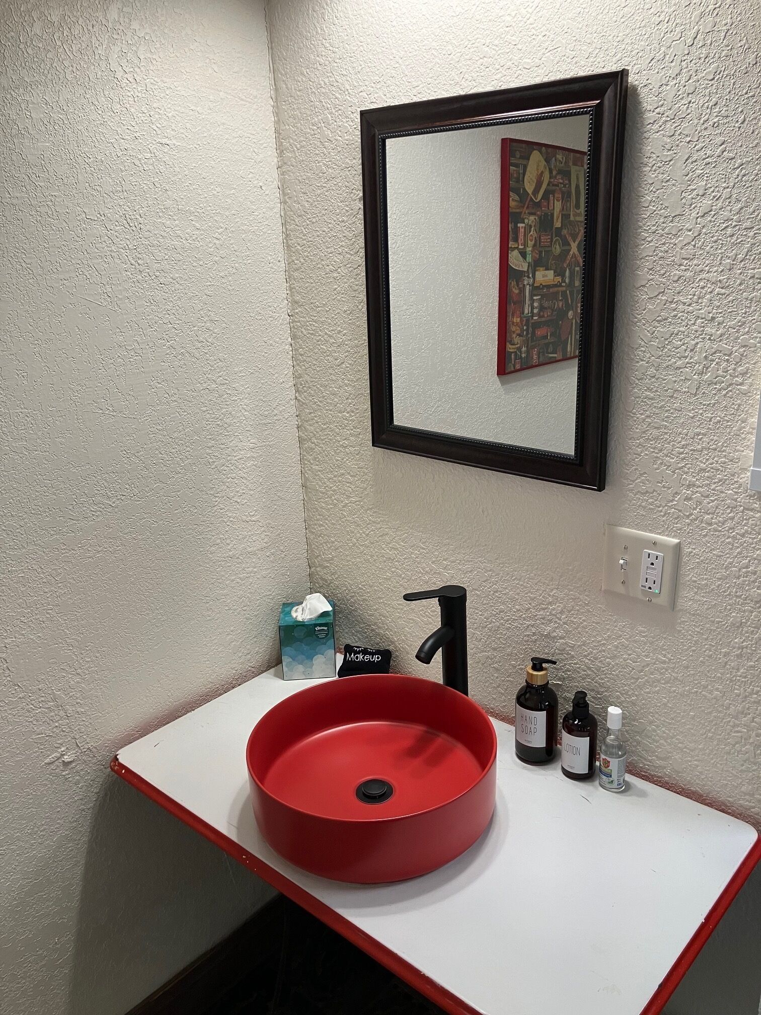 A bathroom with a red sink, a black faucet, a mirror, and toiletries on the counter.