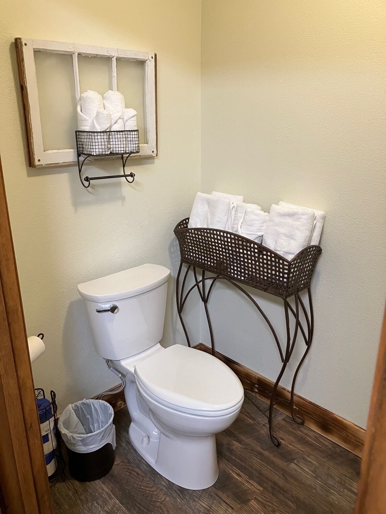 A bathroom with a toilet, a bidet, a trash bin, and a towel rack with towels.