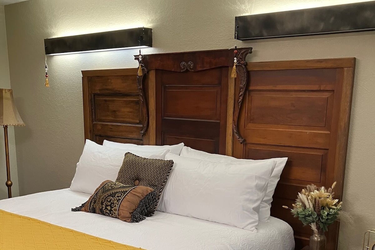 Cama bem arrumada com um cobertor amarelo, cabeceira de madeira e mesa de cabeceira com um vaso de flores.