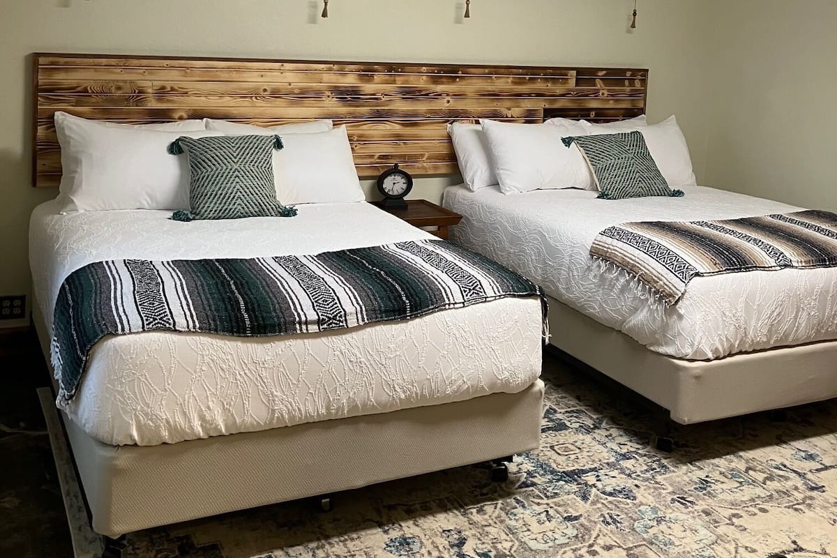 Duas camas de solteiro com cabeceiras de madeira, roupa de cama branca e cobertores decorados.