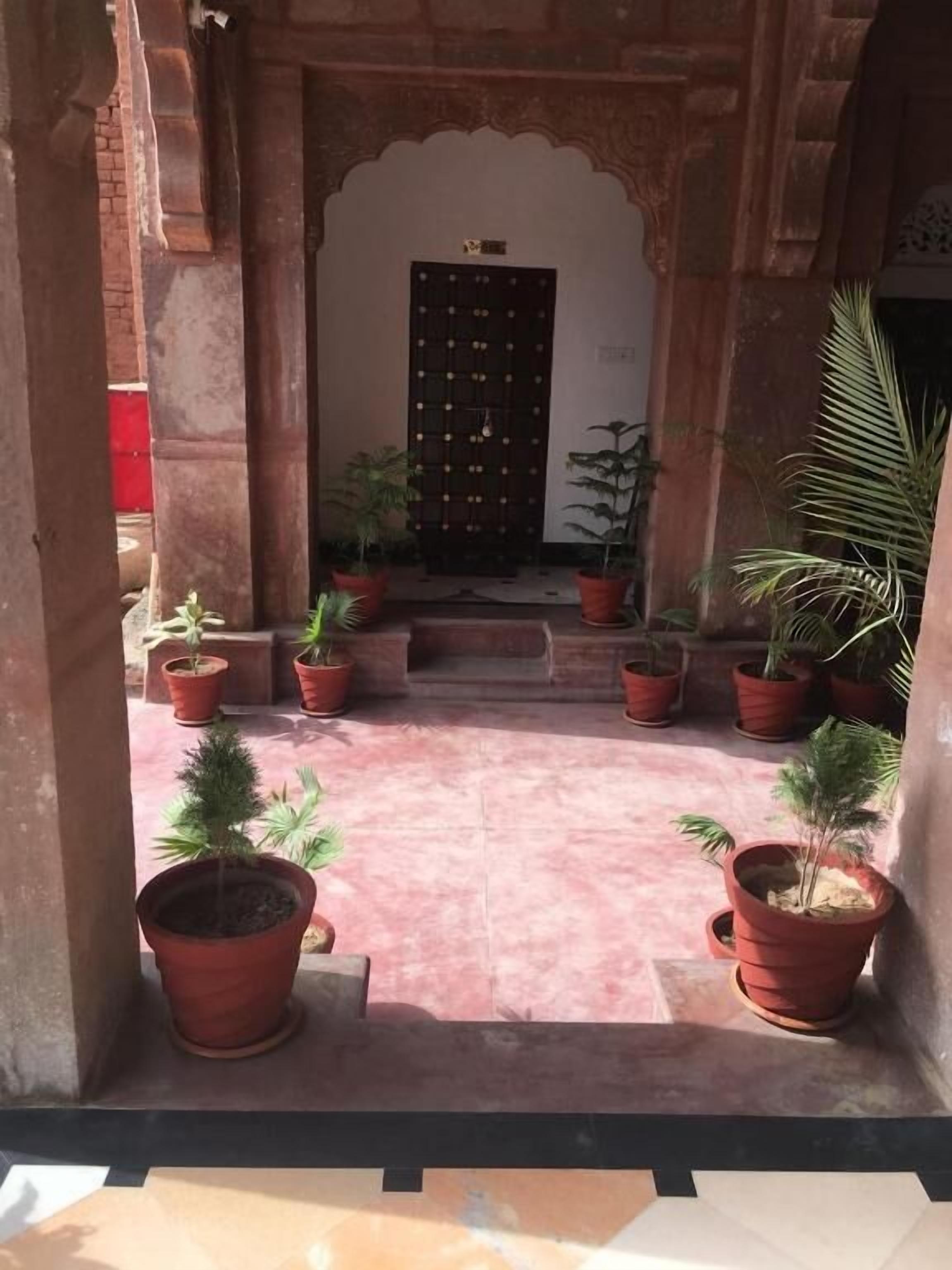 A courtyard with a central door, surrounded by potted plants and a tiled floor.